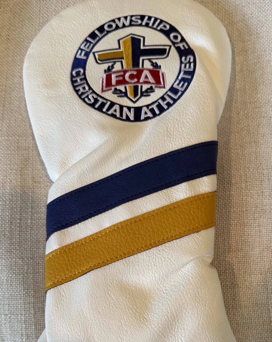 A white driver headcover embroidered with the Fellowship of Christian Athletes crest above navy and gold stripes