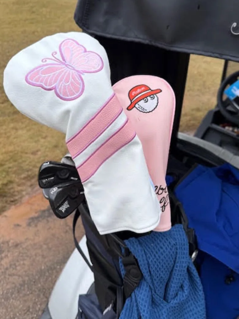 Pink and white headcovers with a butterfly, made for Sadie's Invitational, in a golf bag